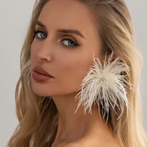 Détail de grandes boucles d'oreilles en plumes d'autruche blanches avec un strass central