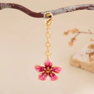 Vue détaillée d'une breloque fleur en émail rose avec chaîne dorée et fermoir mousqueton.