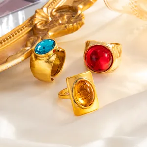 Detail view of three vintage chunky gold rings with blue, red, and amber gemstones on silk.