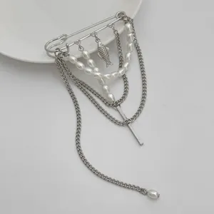 Detail van zilveren kwastjesbroche met parels, vis-hanger en minimalistische kettingen.