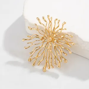 Détail d'une broche dorée en forme de corail organique avec un motif solaire rayonnant.