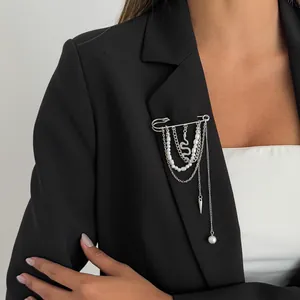 Detailweergave van een zilverkleurige kwastjesbroche met parels en slangenhanger op een blazer.