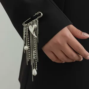 Detailed view of a silver heart tassel safety pin brooch on a black suit sleeve.