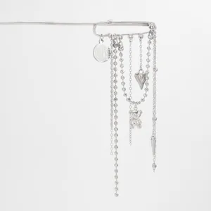 Macro detail of a silver safety pin brooch featuring heart, bear and tassel charms