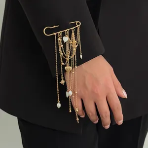 Detailed view of gold safety pin brooch with heart charms and layered chain tassels.