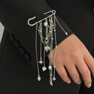 Close-up view of a silver safety pin brooch featuring heart and pearl tassels on a black sleeve.