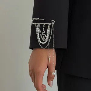 Detailopname van een zilveren gelaagde kwastjesbroche met parels op een zwarte colbertmouw.