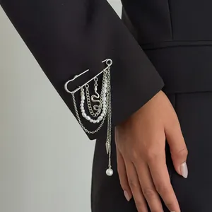 Detailopname van een zilveren veiligheidsspeld broche met parels en slangenkettingen.