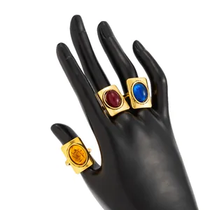 Detail view of vintage gold rings with large oval red, blue, and yellow gemstones on a black hand.