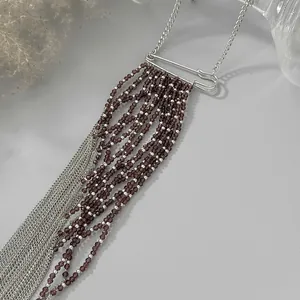 Dettaglio di una collana con design a spilla, perline di cristallo viola e catene argentate.