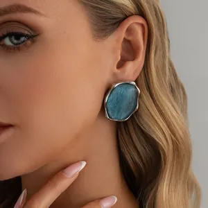 Orecchino geometrico grande con texture a onde blu e cornice argento su modella