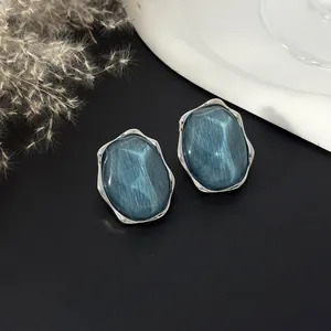 Dettaglio macro di orecchini geometrici con motivo a onde blu scuro e montatura in argento.