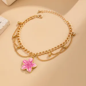 Close-up of golden multi-layer anklet featuring a pink enamel flower pendant