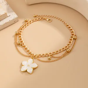 Detail view of a stylish layered gold anklet featuring a delicate white enamel flower charm