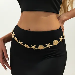 Detail van een bohemien gouden zeester- en schelpenlichaamsketting gedragen op een zwarte jurk