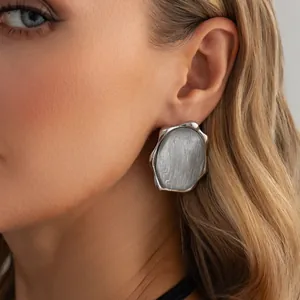 Dettaglio di orecchini geometrici argentati con intarsio grigio su una modella