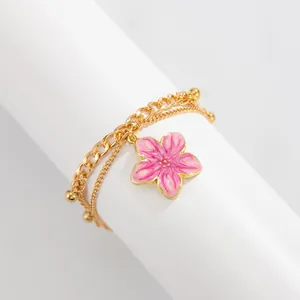 Detailed close-up of a double-layered gold chain anklet featuring a pink enamel flower