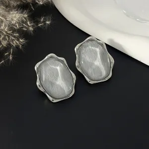 Dettaglio di orecchini color argento con intarsio in pietra grigia e bordo a onde
