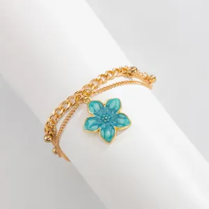 Detailed shot of a gold layered anklet featuring a vibrant blue enamel flower charm