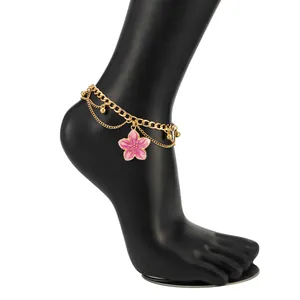 Detailed close-up of a gold layered anklet with pink enamel flower on black mannequin