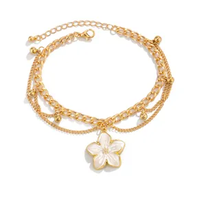 Detail of a gold-tone layered anklet featuring a delicate white enamel flower pendant.