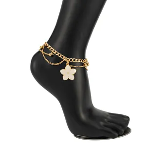 Detail of a beach holiday style anklet with a white enamel flower charm and gold chains.