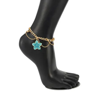 Close-up detail of a double-layered gold anklet with a blue enamel flower charm.