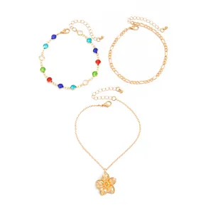 Detail of three gold-tone anklets featuring a flower pendant and colorful beads on white.