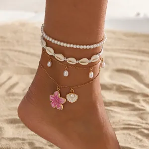 Detail view of boho beach anklet set featuring pink flower and shell charms on sand