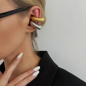 Model wearing gold and silver ribbed stainless steel C-shaped ear cuffs on cartilage