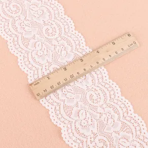 Detailansicht der breiten weißen elastischen Spitzenborte mit Blumenmuster und Lineal