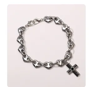 Gros plan du bracelet à maillons cœur en acier avec pendentif croix noire cloutée.