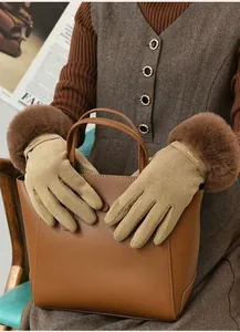 Detail of khaki winter gloves with brown faux fur trim and gold metal logo plate.