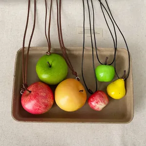 Collares con colgantes de manzana y pera simulados únicos en una bandeja de papel rústica.