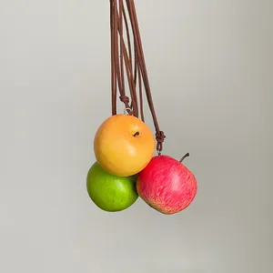 Primer plano de tres colgantes de manzana realistas en rojo, amarillo y verde con cuerdas.
