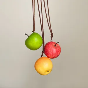 Vista detallada de tres colgantes de manzana simulada en rojo, verde y amarillo