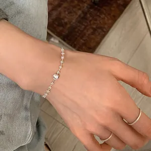Détail d'un bracelet en argent minimaliste avec boule brossée et bagues sur la main