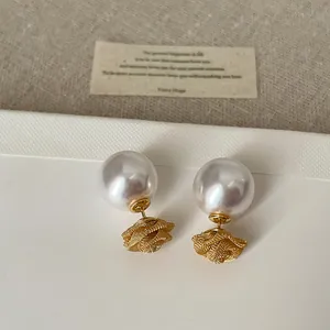 Détail d'élégantes boucles d'oreilles double face rose en maille dorée et perle blanche