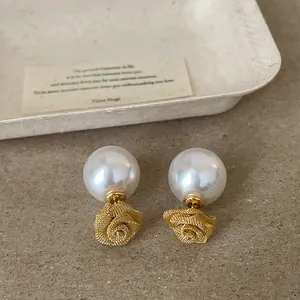 Détail rapproché de la rose en résille dorée et des boucles d'oreilles en perles blanches.
