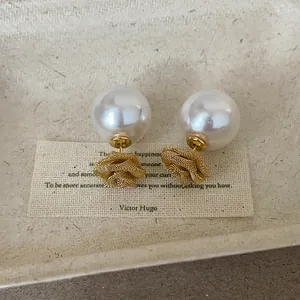 Gros plan de boucles d'oreilles en maille dorée et perles blanches sur carte.