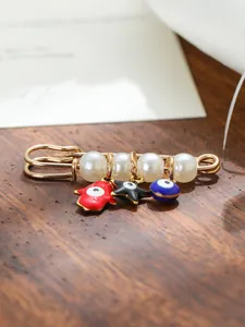 Detail view of ethnic brooch featuring pearls, red Hamsa hand, and blue Evil Eye charm