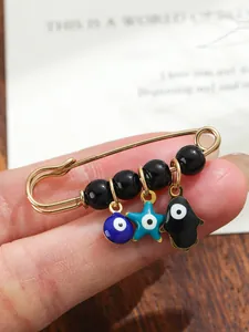 Detailed view of evil eye and Hamsa hand charms on a gold-plated safety pin brooch.