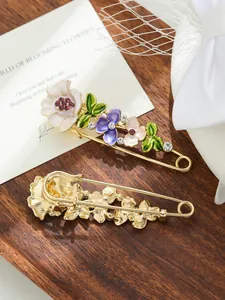 Dettaglio ravvicinato di una spilla a balia dorata con fiori in smalto colorato