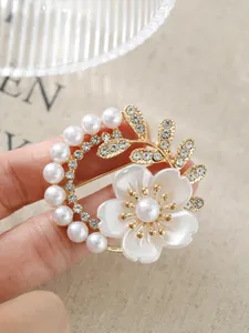 Nahaufnahme einer eleganten, goldfarbenen Blumenbrosche mit weißen Perlen und Strass