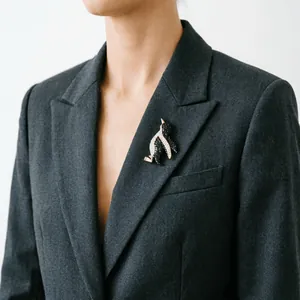 Detailed view of a sparkling crystal penguin brooch worn on a dark grey blazer lapel
