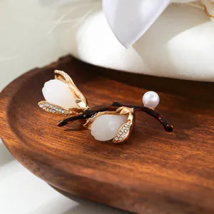 Close-up of white magnolia brooch with pearl and crystals resting on a polished wood plate