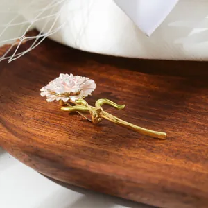 Detailed view of a pink carnation brooch with gold-plated stem on a wooden tray.