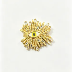 Detail of a gold sunburst evil eye brooch with crystal accents on white background.