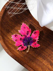 Nahaufnahme einer pink-violetten Ahornblatt-Brosche mit Strasssteinen auf Holztablett