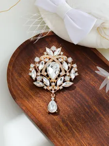 Close-up of vintage crystal rhinestone brooch with teardrop pendant on wood tray.